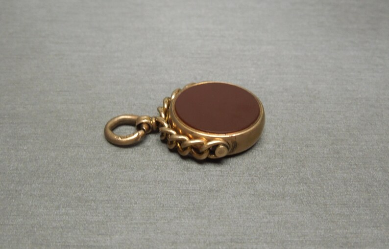 May include: A gold-toned pocket watch fob with a brown carnelian stone and a chain.