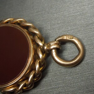 May include: A gold fob chain with a brown cameo set in a gold bezel. The chain has a ring at the end with the hallmark "9375" stamped on it.