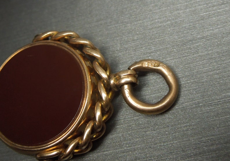 May include: A gold fob chain with a brown cameo set in a gold bezel. The chain has a ring at the end with the hallmark "9375" stamped on it.