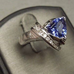 May include: A silver ring with a large, blue, triangular-shaped gemstone surrounded by smaller, white gemstones.