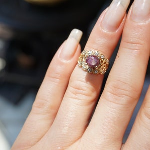 May include: A gold ring with a pink gemstone surrounded by smaller clear gemstones.