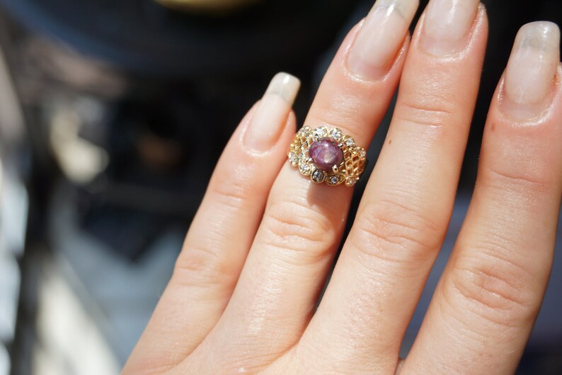 May include: A gold ring with a pink gemstone surrounded by smaller clear gemstones.