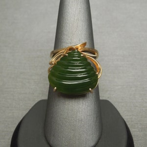 以下が含まれることがあります： 繊細な渦巻き模様にセットされた、大きな緑色の翡翠の石がついた金の指輪。翡翠の石は同心円状に彫刻されており、ユニークでエレガントな外観を与えています。