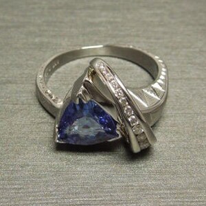 May include: A silver ring with a triangular blue gemstone and a row of small diamonds set in the band.