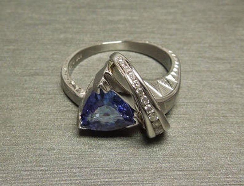 May include: A silver ring with a triangular blue gemstone and a row of small diamonds set in the band.