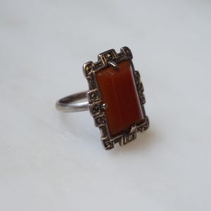 May include: A silver ring with a rectangular carnelian stone set in a geometric frame of marcasite.