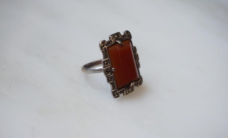 May include: A silver ring with a rectangular carnelian stone set in a geometric frame of marcasite.