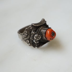 May include: A silver ring with an intricate design and a bright orange coral stone.