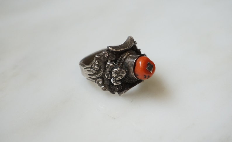 May include: A silver ring with an intricate design and a bright orange coral stone.