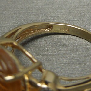 May include: Gold ring with a large, oval-shaped amber stone set in a delicate, intricate design. The ring is marked "10K" on the inside band.