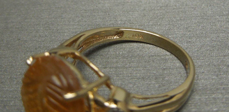 May include: Gold ring with a large, oval-shaped amber stone set in a delicate, intricate design. The ring is marked "10K" on the inside band.
