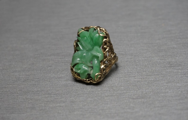 May include: A green jade ring set in a gold filigree design. The jade is carved into a floral pattern.