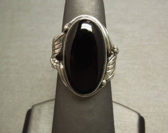 May include: A silver ring with an oval black onyx stone set in a detailed silver design.