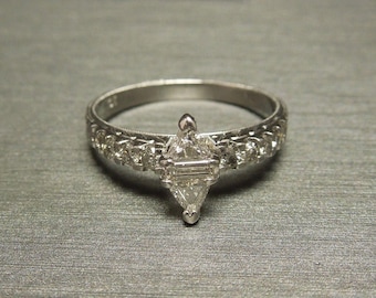 Pode incluir: Um anel de prata com um grande diamante triangular transparente engastado no centro. A banda é decorada com diamantes menores.