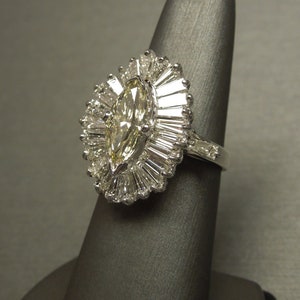 Op de afbeelding: Een ring van witgoud met een marquise-geslepen diamant en een halo van baguette-geslepen diamanten.