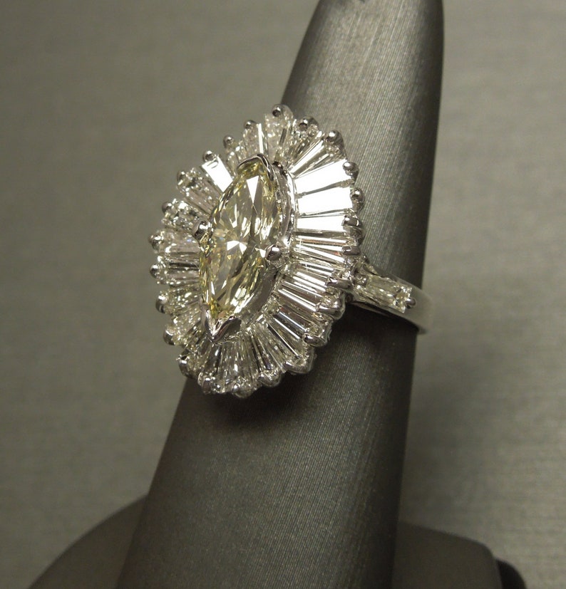 Op de afbeelding: Een ring van witgoud met een marquise-geslepen diamant en een halo van baguette-geslepen diamanten.