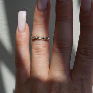 May include: A gold ring featuring a repeating diamond design. The ring is worn on a finger, with the image showing the ring's details and the skin's texture. The ring is a delicate piece of jewellery, suitable for everyday wear.