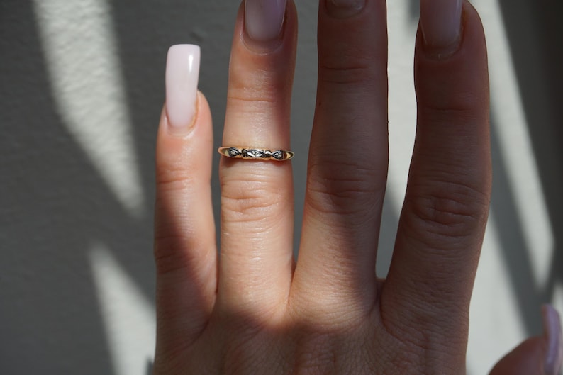 May include: A gold ring featuring a repeating diamond design. The ring is worn on a finger, with the image showing the ring's details and the skin's texture. The ring is a delicate piece of jewellery, suitable for everyday wear.