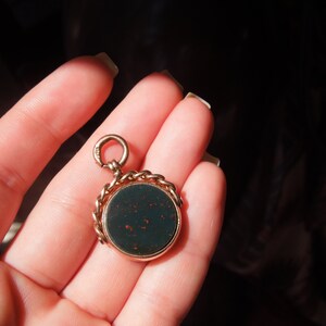 May include: A gold chain fob with a dark green cameo. The cameo is set in a gold frame and has a detailed design.
