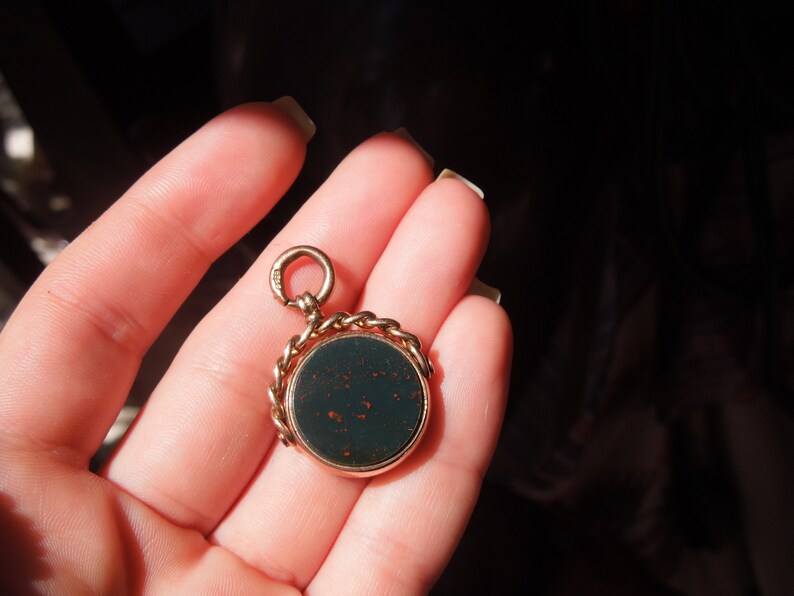 May include: A gold chain fob with a dark green cameo. The cameo is set in a gold frame and has a detailed design.