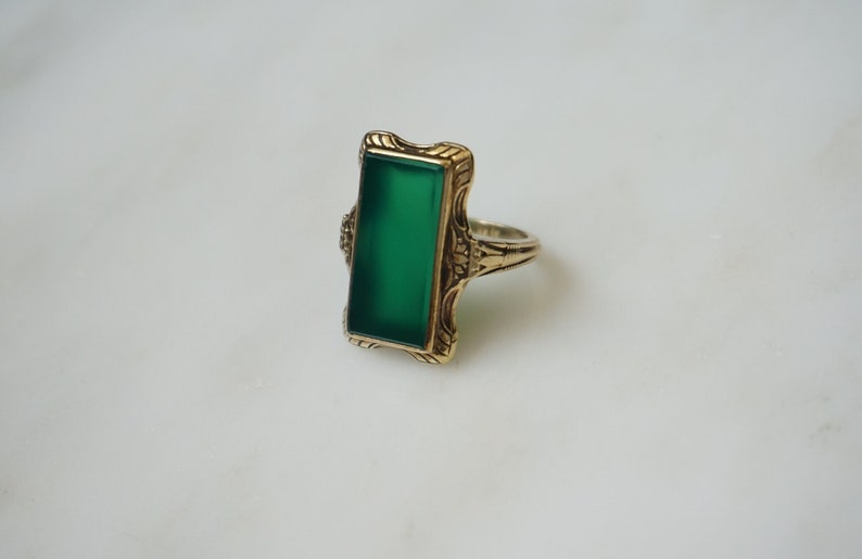 May include: A gold ring with a green rectangular stone set in a filigree design.