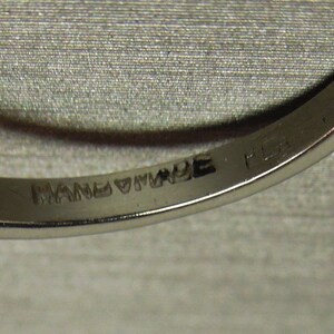 以下が含まれることがあります： 内側に「HANDMADE」と「PLAT. IN」の刻印が施された銀の指輪のクローズアップ。