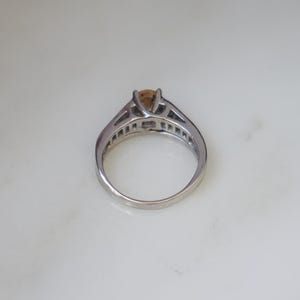 Pode incluir: Um anel de prata com uma gema marrom engastada em garras. O anel tem uma banda delicada com pequenas pedras engastadas em pav&eacute;.