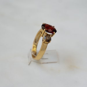 May include: A gold ring with a large red gemstone and two smaller clear gemstones.