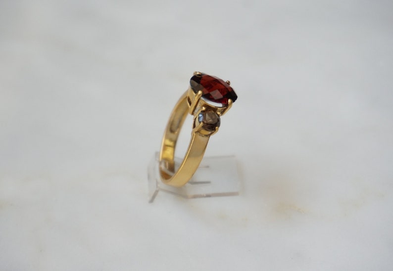 May include: A gold ring with a large red gemstone and two smaller clear gemstones.