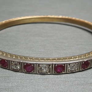 May include: A gold and silver bangle bracelet with a row of red rubies and diamonds set in a decorative design.