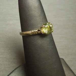 May include: A gold ring with a round, light green gemstone. The ring has a textured band.