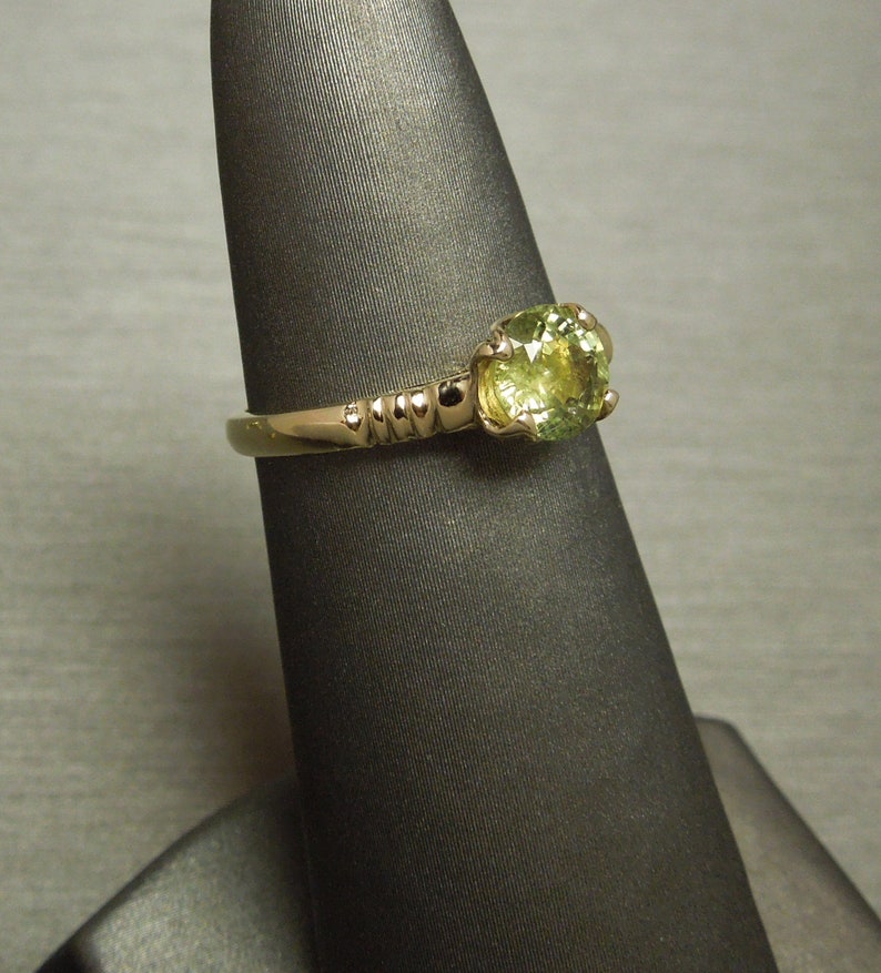 May include: A gold ring with a round, light green gemstone. The ring has a textured band.