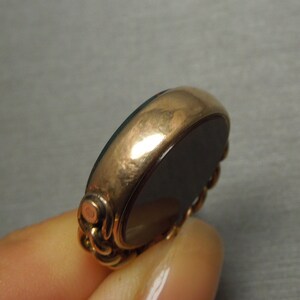 May include: A gold-toned ring with a black oval gemstone. The ring has a detailed design around the gemstone.