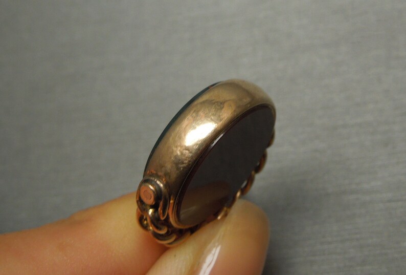 May include: A gold-toned ring with a black oval gemstone. The ring has a detailed design around the gemstone.