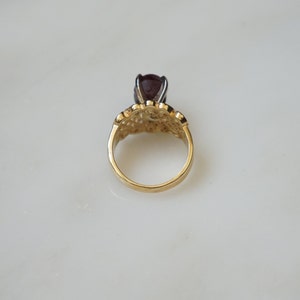 May include: A gold ring with a dark red gemstone set in a filigree design.