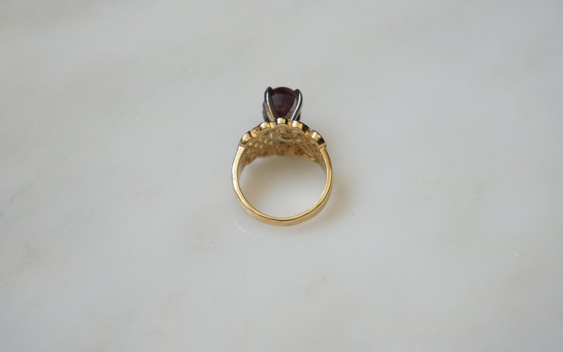 May include: A gold ring with a dark red gemstone set in a filigree design.