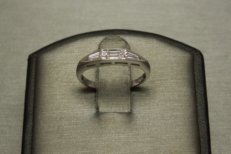 May include: A silver band ring with five small, clear, rectangular-shaped diamonds set in a row.