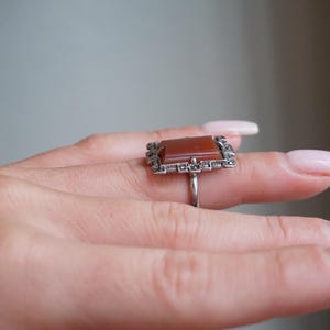 May include: A silver ring with a rectangular carnelian stone set in a frame of marcasite stones.