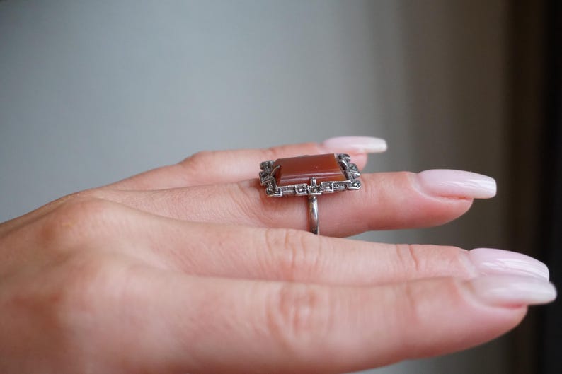 May include: A silver ring with a rectangular carnelian stone set in a frame of marcasite stones.