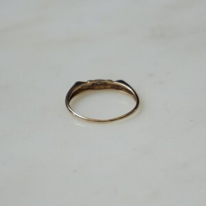 May include: A gold ring with a small, decorative top. The ring has a simple band and a slightly raised, detailed design on the top. The ring is set against a white background.