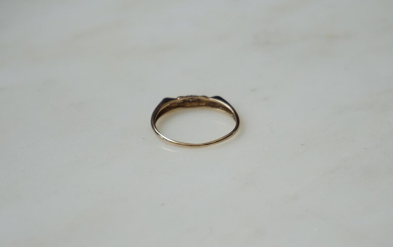 May include: A gold ring with a small, decorative top. The ring has a simple band and a slightly raised, detailed design on the top. The ring is set against a white background.