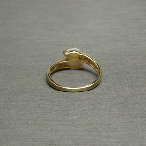 K&ouml;nnte beinhalten: Ein goldener Ring mit einem wei&szlig;en ovalen Edelstein, der in der Mitte sitzt. Der Ring hat eine Band aus kleinen Diamanten, die in einer Pav&eacute;-Fassung sitzen.