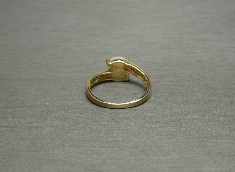 K&ouml;nnte beinhalten: Ein goldener Ring mit einem wei&szlig;en ovalen Edelstein, der in der Mitte sitzt. Der Ring hat eine Band aus kleinen Diamanten, die in einer Pav&eacute;-Fassung sitzen.