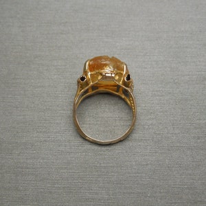 Op de afbeelding: Een gouden ring met een grote, oranje edelsteen in een bezel-setting. De ring heeft een delicaat, versierd ontwerp.