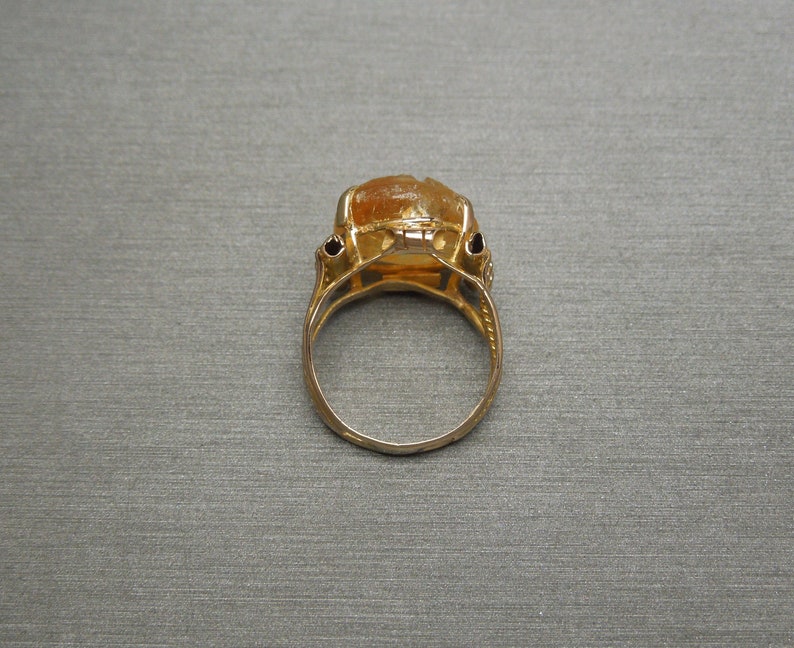 Op de afbeelding: Een gouden ring met een grote, oranje edelsteen in een bezel-setting. De ring heeft een delicaat, versierd ontwerp.