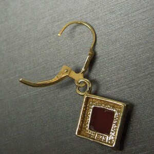 May include: Gold tone dangle earrings with a square red stone set in a gold tone frame. The earrings have a 925 stamp on the back.