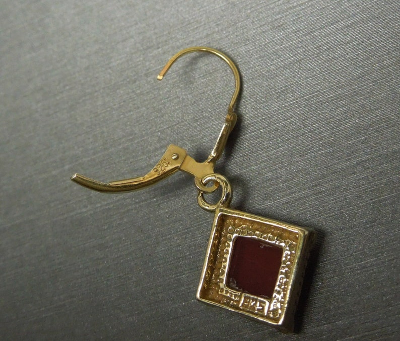 May include: Gold tone dangle earrings with a square red stone set in a gold tone frame. The earrings have a 925 stamp on the back.