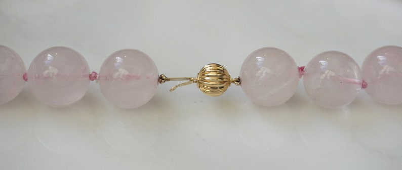 May include: A pink rose quartz necklace with a gold clasp. The necklace is made of large, round beads.