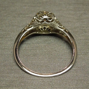 Puede incluir: Un anillo de compromiso de filigrana de plata con una piedra central redonda. El anillo se muestra desde abajo, mostrando los intrincados detalles de la banda.