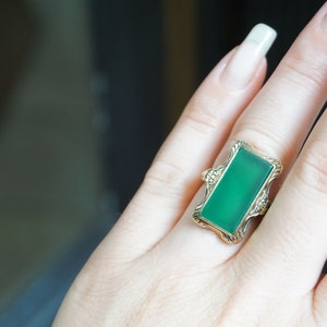 May include: A gold ring with a rectangular green gemstone set in a decorative frame.
